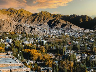 A stunning aerial view of Leh city surrounded by majestic mountains and colorful autumn foliage.