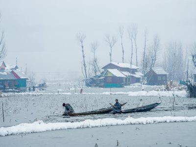 Two individuals paddle through snowy landscapes in Kashmir, showcasing the serene winter beauty.