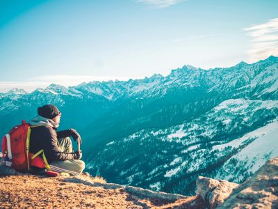 A lone backpacker sitting on a mountain summit admiring the snowy peaks of the Himalayas.